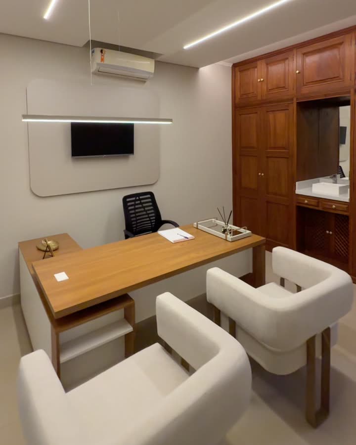 Consultório com mesa de madeira e poltronas brancas
